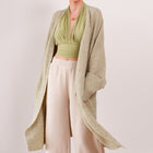 OKAKIE Etoile soft modal drape cardigan in a beige knit, worn open over a green halter top and cream trousers.