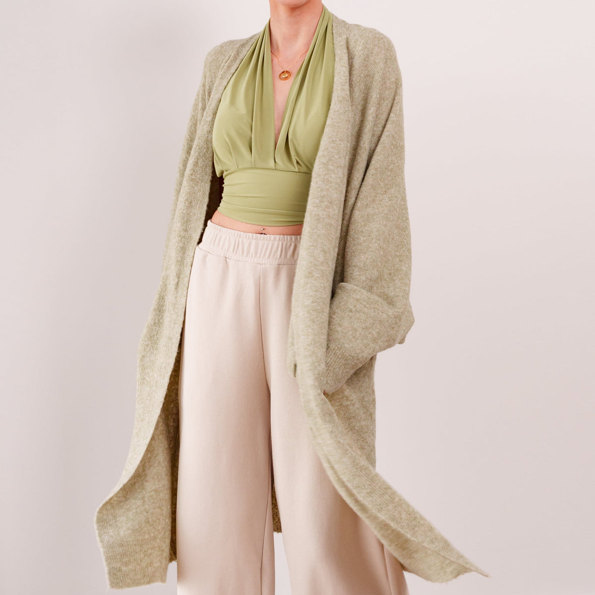 OKAKIE Etoile soft modal drape cardigan in a beige knit, worn open over a green halter top and cream trousers.