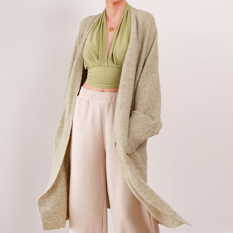 OKAKIE Etoile soft modal drape cardigan in a beige knit, worn open over a green halter top and cream trousers.