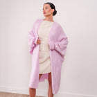 Model wearing an OKAKIE soft pink cotton-modal maxi cardigan with voluminous sleeves over a cream dress