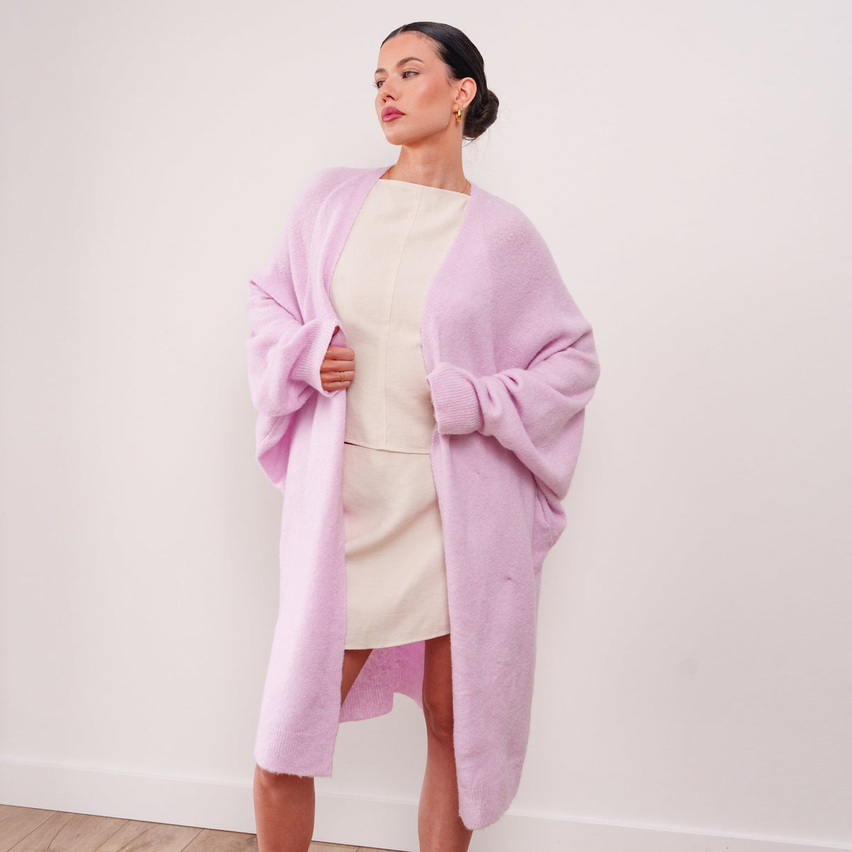 Model wearing an OKAKIE soft pink cotton-modal maxi cardigan with voluminous sleeves over a cream dress