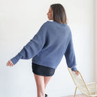 OKAKIE model wearing a fuzzy blue mock-neck tunic with voluminous sleeves and dropped shoulders, back view.