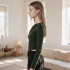 Model wearing OKAKIE dark green ribbed asymmetric draped sweater top with long sleeves in a bright minimalist room.