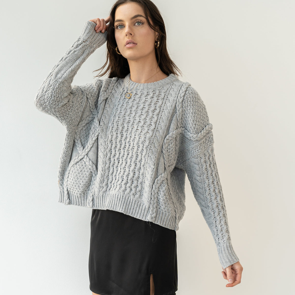 OKAKIE model wearing a grey oversized 100% cotton cable-knit sweater with a crew neck and textured braided patterns.