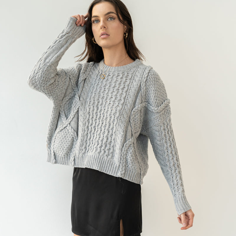 OKAKIE model wearing a grey oversized 100% cotton cable-knit sweater with a crew neck and textured braided patterns.