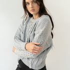 Model wearing an OKAKIE grey heavyweight cotton cable-knit sweater with a crew neckline and oversized fit.