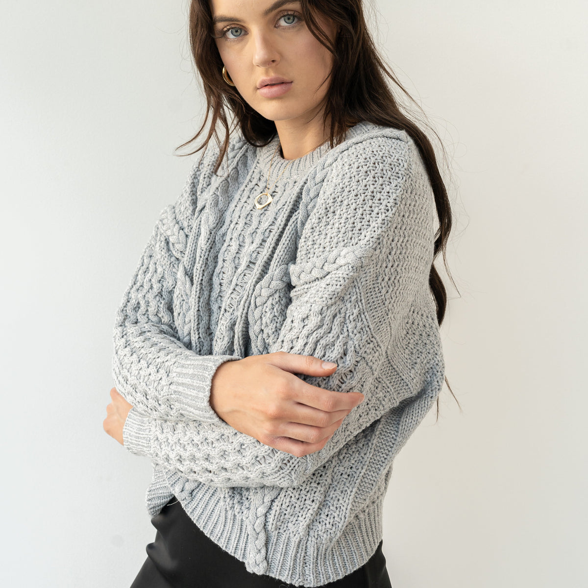 Model wearing an OKAKIE grey heavyweight cotton cable-knit sweater with a crew neckline and oversized fit.