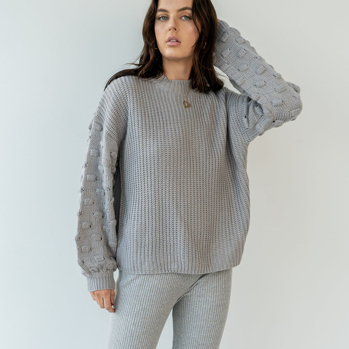 OKAKIE grey crew neck sweater featuring a ribbed body and dimensional popcorn knit sleeves on a model