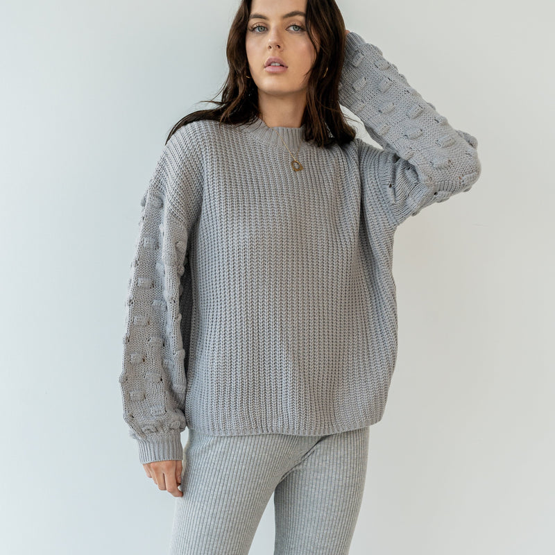 OKAKIE grey crew neck sweater featuring a ribbed body and dimensional popcorn knit sleeves on a model