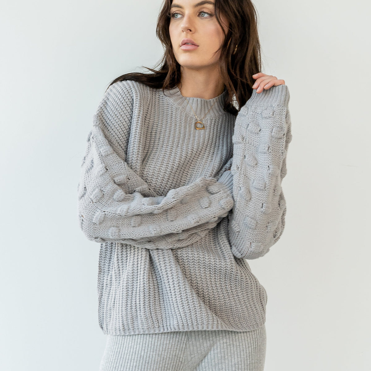 OKAKIE Solène grey crew neck sweater with textured popcorn knit sleeves and ribbed body on a model