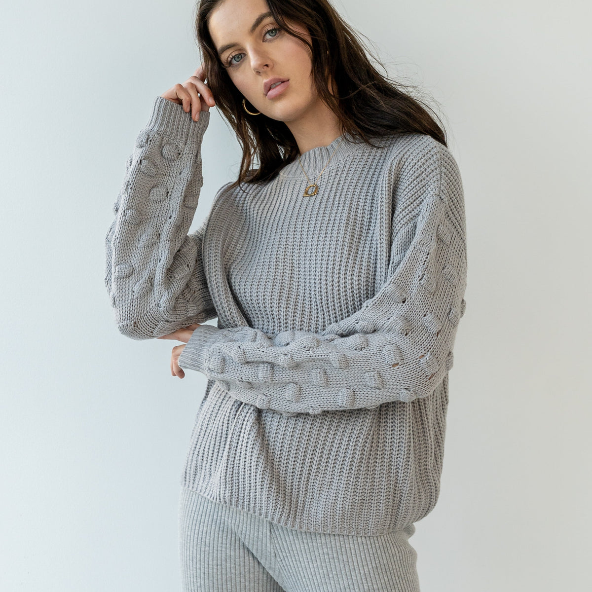 OKAKIE grey crew neck sweater with textured popcorn knit sleeves and ribbed body on a model