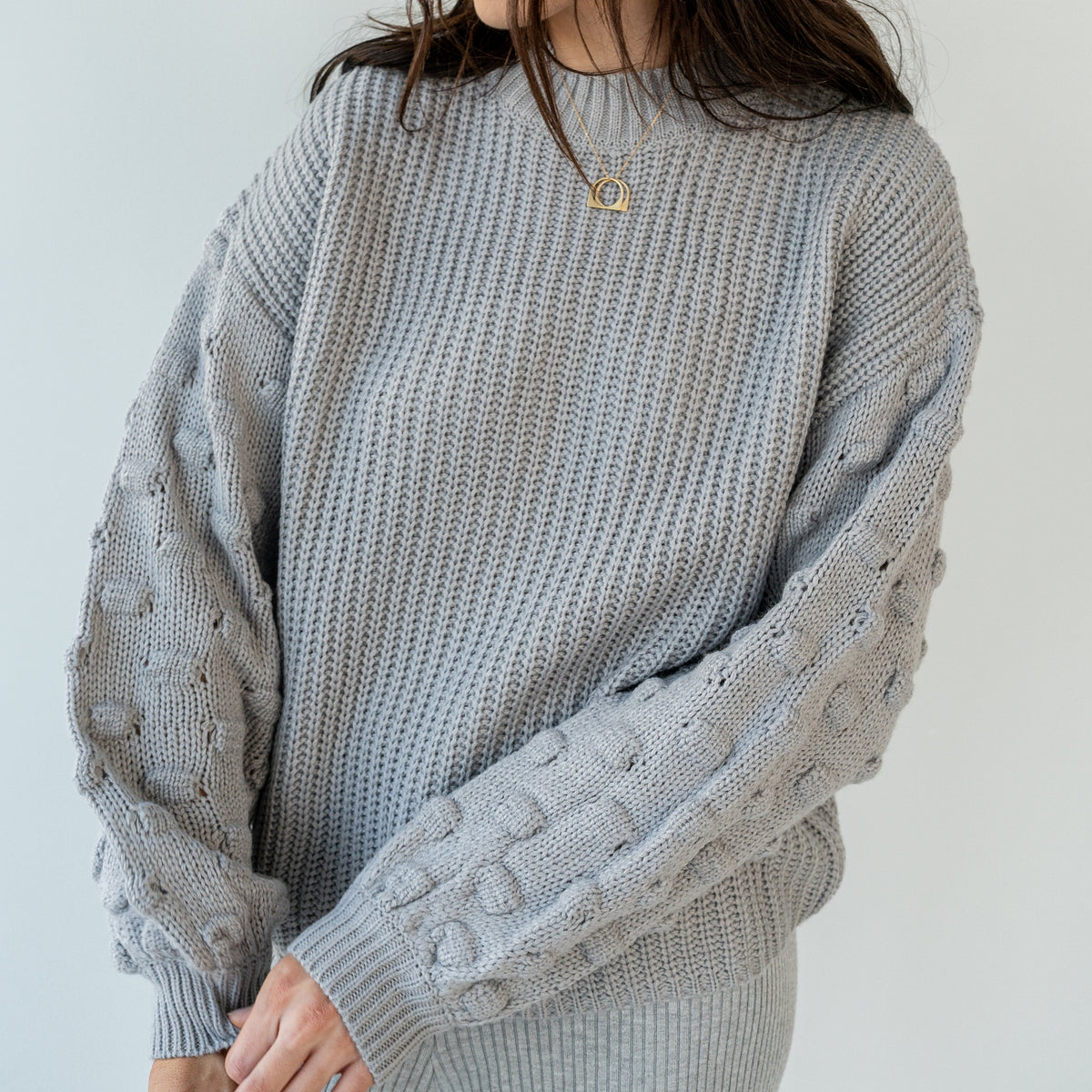 OKAKIE grey crew neck sweater with ribbed body and textured popcorn knit sleeves on a model
