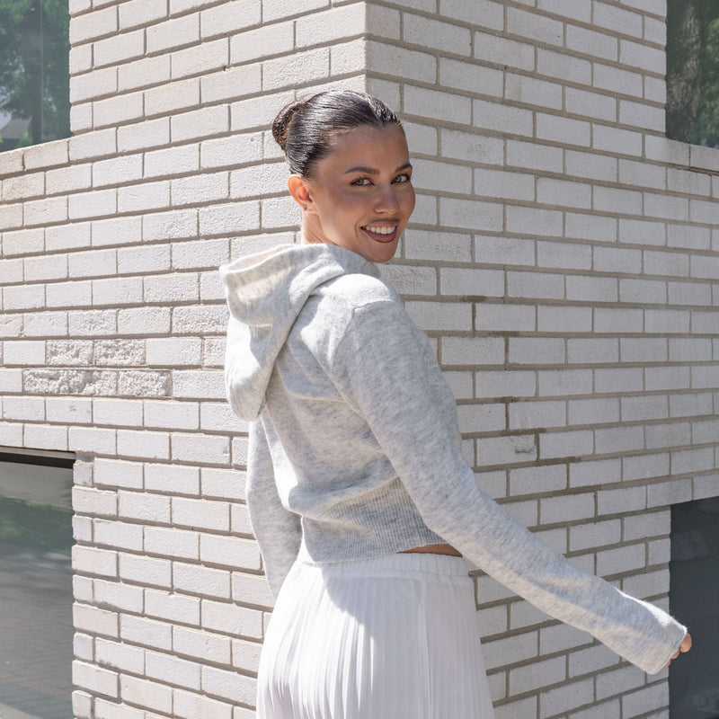 OKAKIE heather grey cotton knit zip hoodie with a relaxed fit and hood, worn by a woman against a brick wall.