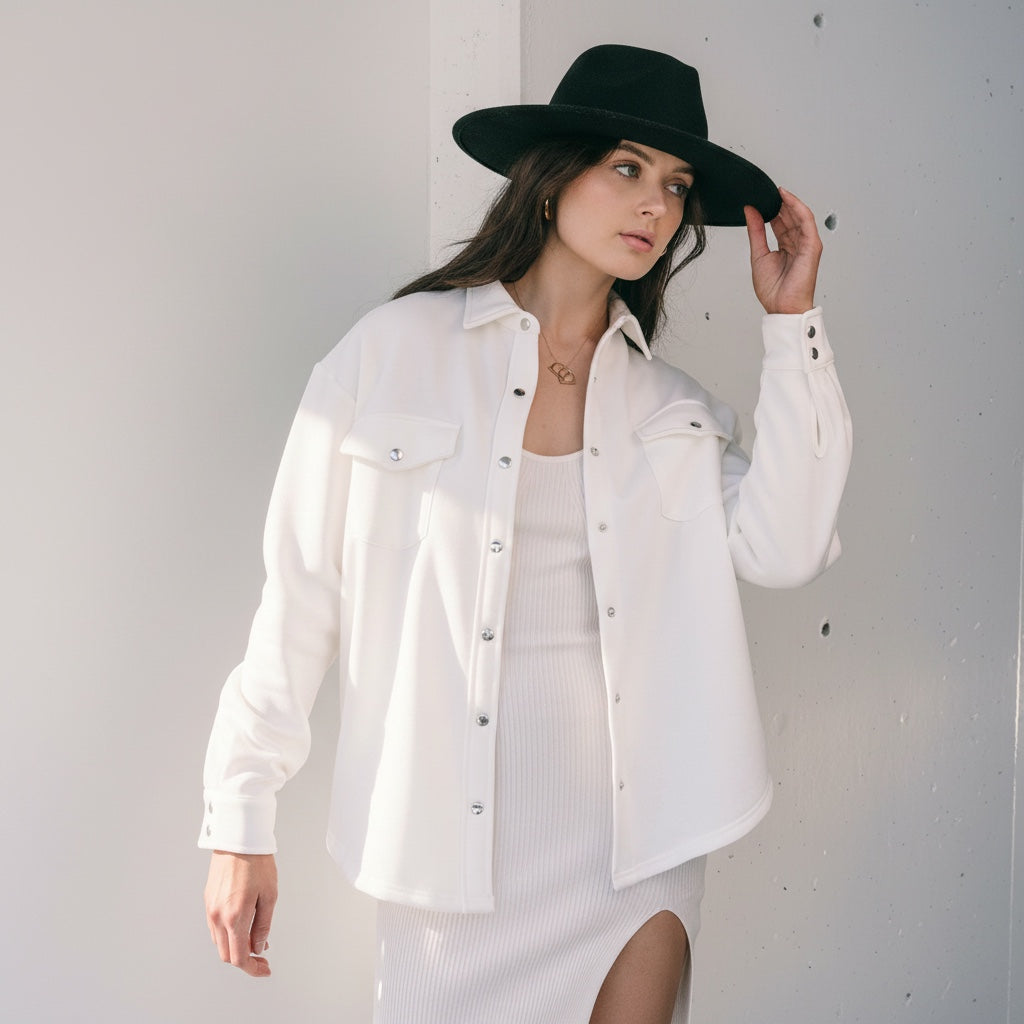OKAKIE ivory cotton snap shacket with silver buttons and chest pockets worn by a woman in a black hat