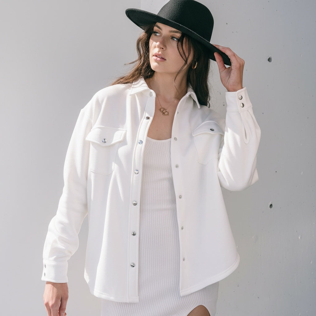 Model wearing an OKAKIE ivory cotton snap shacket with silver buttons and chest pockets over a matching dress.