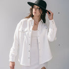 Model wearing an OKAKIE ivory cotton snap shacket with silver buttons and chest pockets over a matching dress.