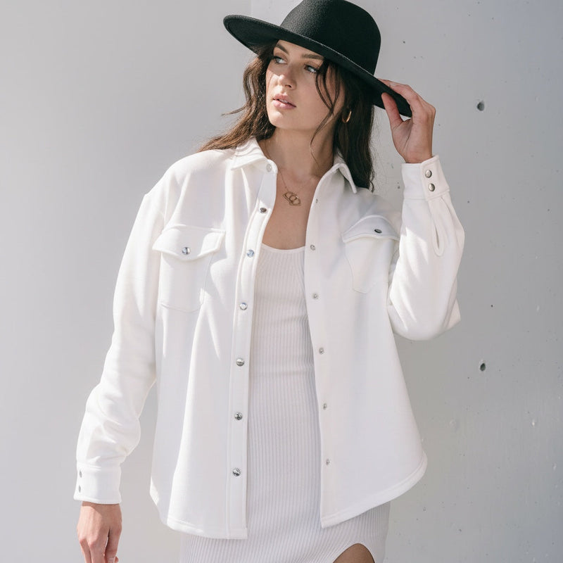 Model wearing an OKAKIE ivory cotton snap shacket with silver buttons and chest pockets over a matching dress.