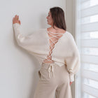 OKAKIE ivory knit sweater featuring a dramatic lace-up back detail, wide sleeves, and a relaxed fit on a model.
