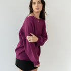 Model wearing an OKAKIE magenta heavyweight tunic sweater with a wide neckline and textured knit, side view.