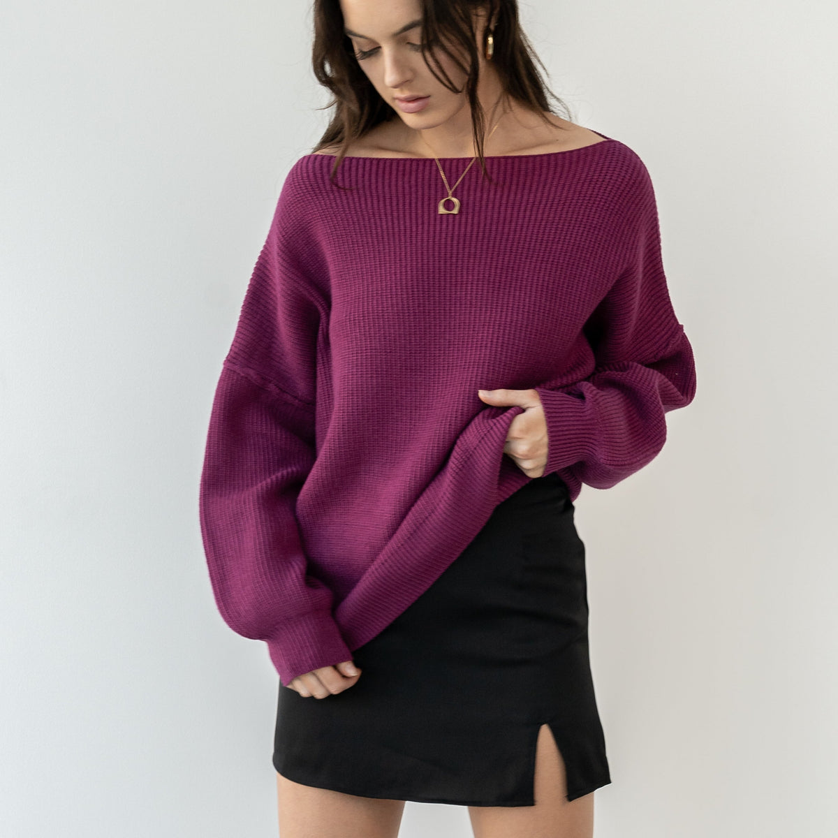 Model wearing an OKAKIE magenta heavyweight tunic sweater with a wide neckline and drop shoulders over a black skirt.