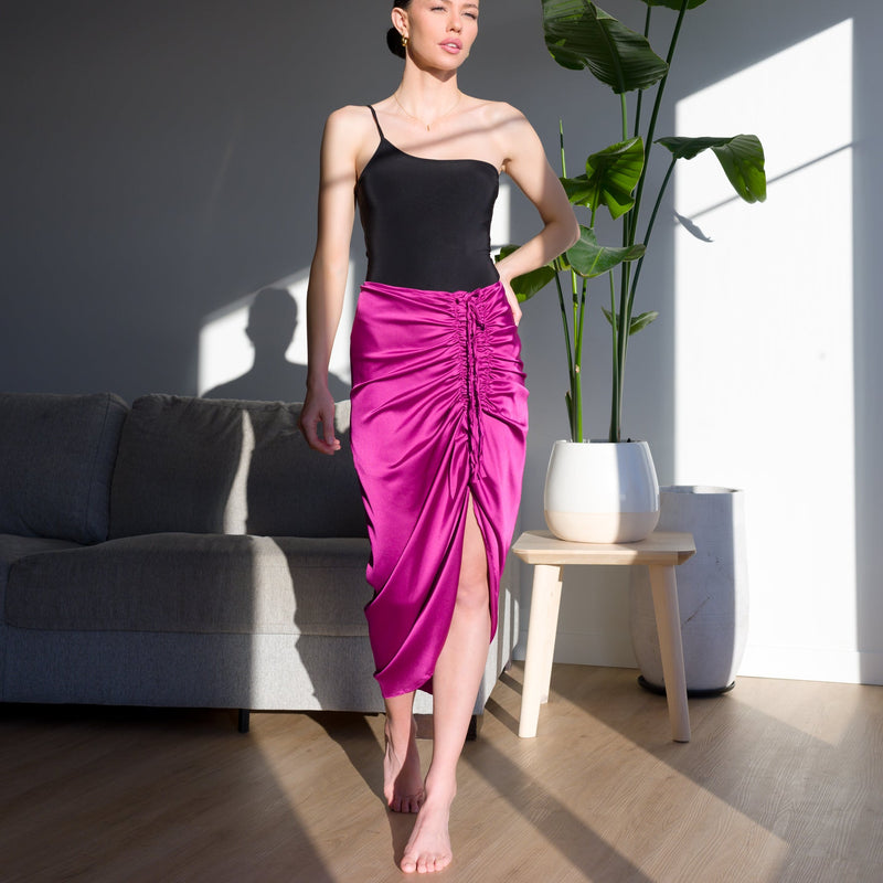 Model wearing OKAKIE magenta stretch satin midi skirt with adjustable centre-front ruching and side slit