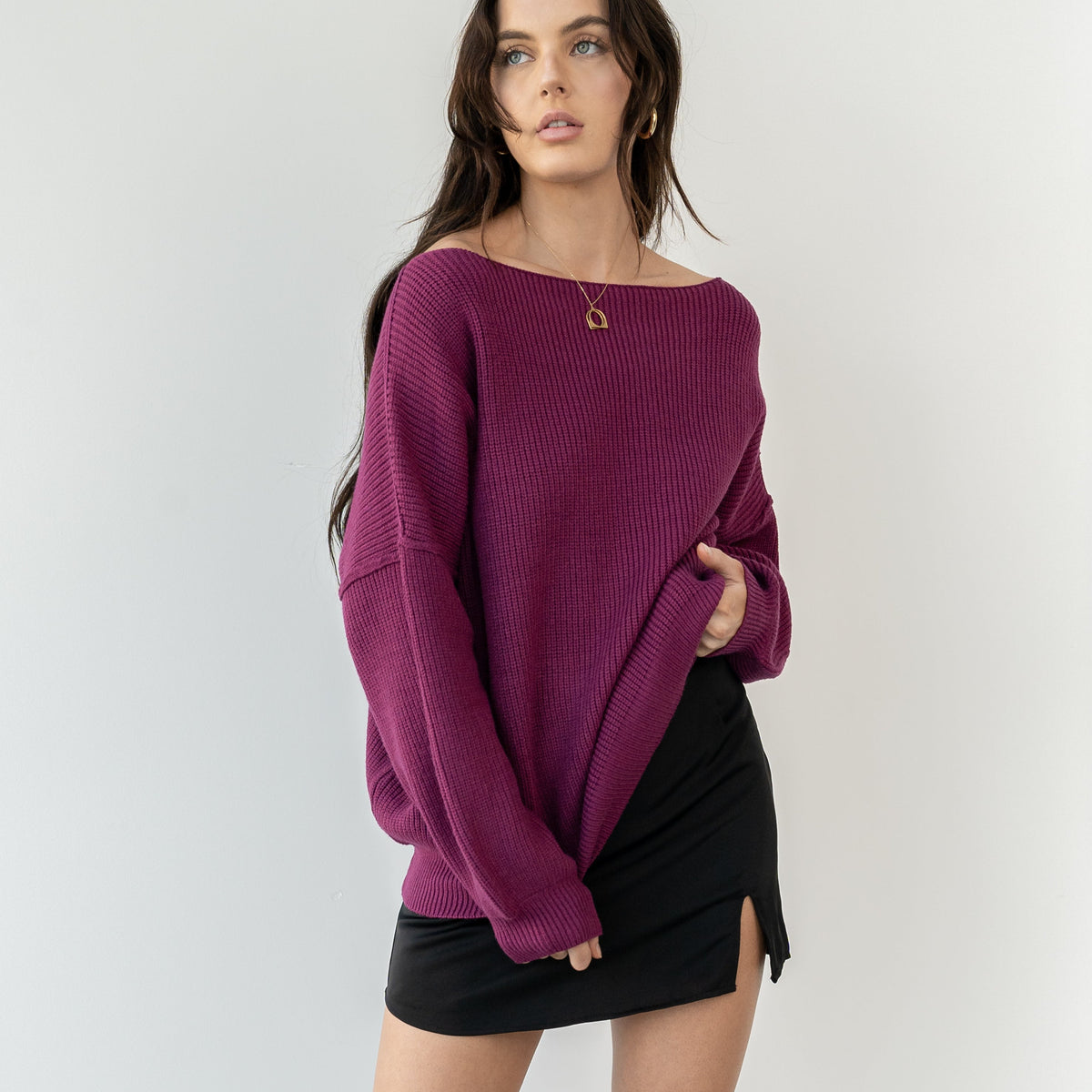 Model wearing OKAKIE magenta heavy tunic knit sweater with wide neckline and drop shoulders against a white wall