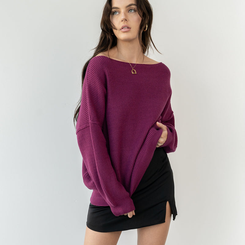 Model wearing OKAKIE magenta heavy tunic knit sweater with wide neckline and drop shoulders against a white wall