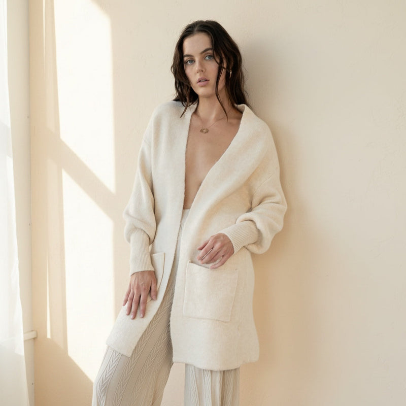 Model wearing OKAKIE Marcelle heavy knit coatigan in cream with shawl collar, oversized pockets, and ribbed cuffs.