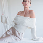 OKAKIE off-shoulder ribbed sweater in cream with a fold-over neckline and long flared sleeves worn by a model.