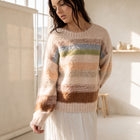 Model wearing an OKAKIE plush pastel striped sweater with a crew neckline and drop shoulders in a sunlit studio.