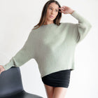 Model wearing an OKAKIE sage green fuzzy mock-neck tunic with relaxed drop shoulders and long sleeves.