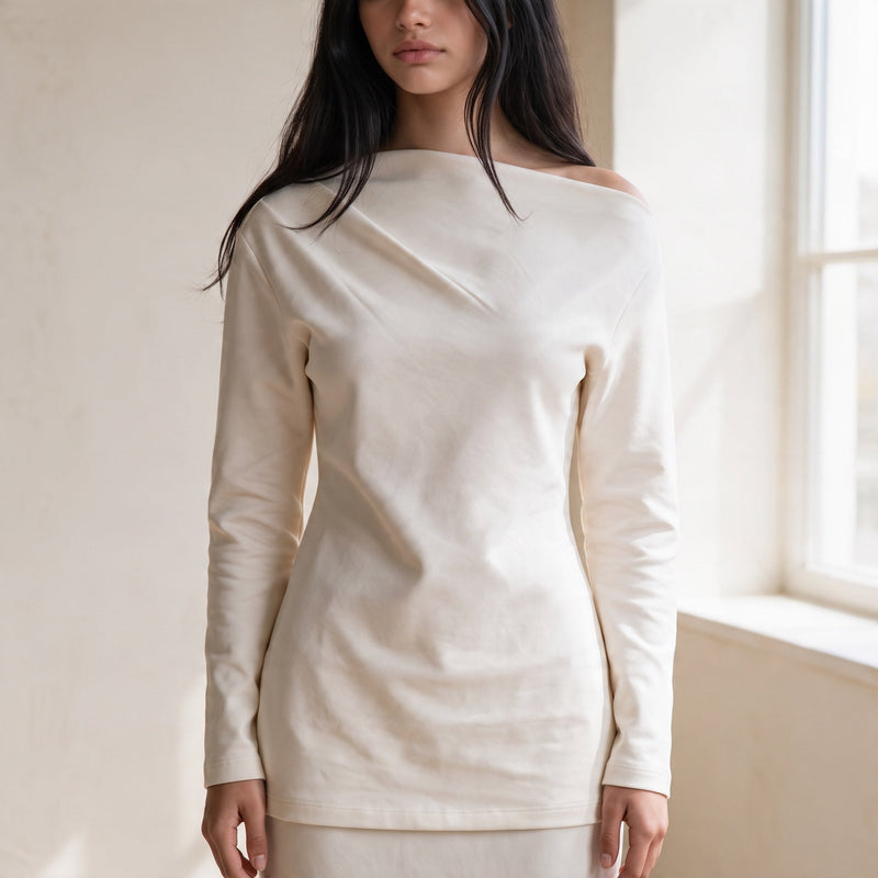 OKAKIE Solène asymmetric scuba knit top in cream with long sleeves and a sculptural off-shoulder neckline.