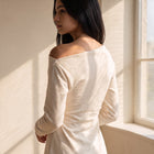OKAKIE Solène asymmetric scuba knit top in cream with long sleeves and off-shoulder neckline on a model