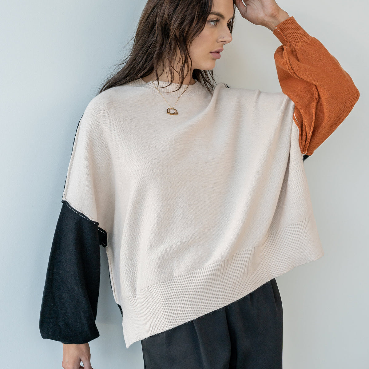 OKAKIE Solène three-tone knit sweater featuring cream body, rust and charcoal sleeves, and relaxed drop-shoulder fit.