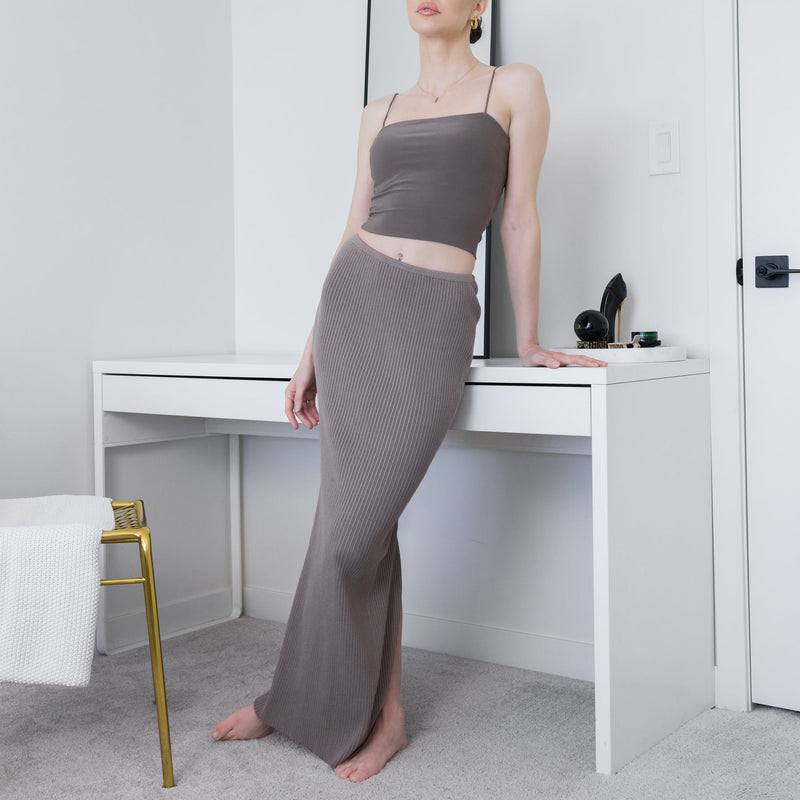 OKAKIE taupe ribbed knit maxi skirt worn with a matching camisole top in a minimalist bedroom setting.