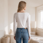OKAKIE white long-sleeve boat neck top with ribbed texture worn by a woman from behind in a bright bedroom.