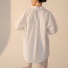 Back view of OKAKIE white cotton poplin boyfriend over-shirt with a loose fit and high-low hem on a model