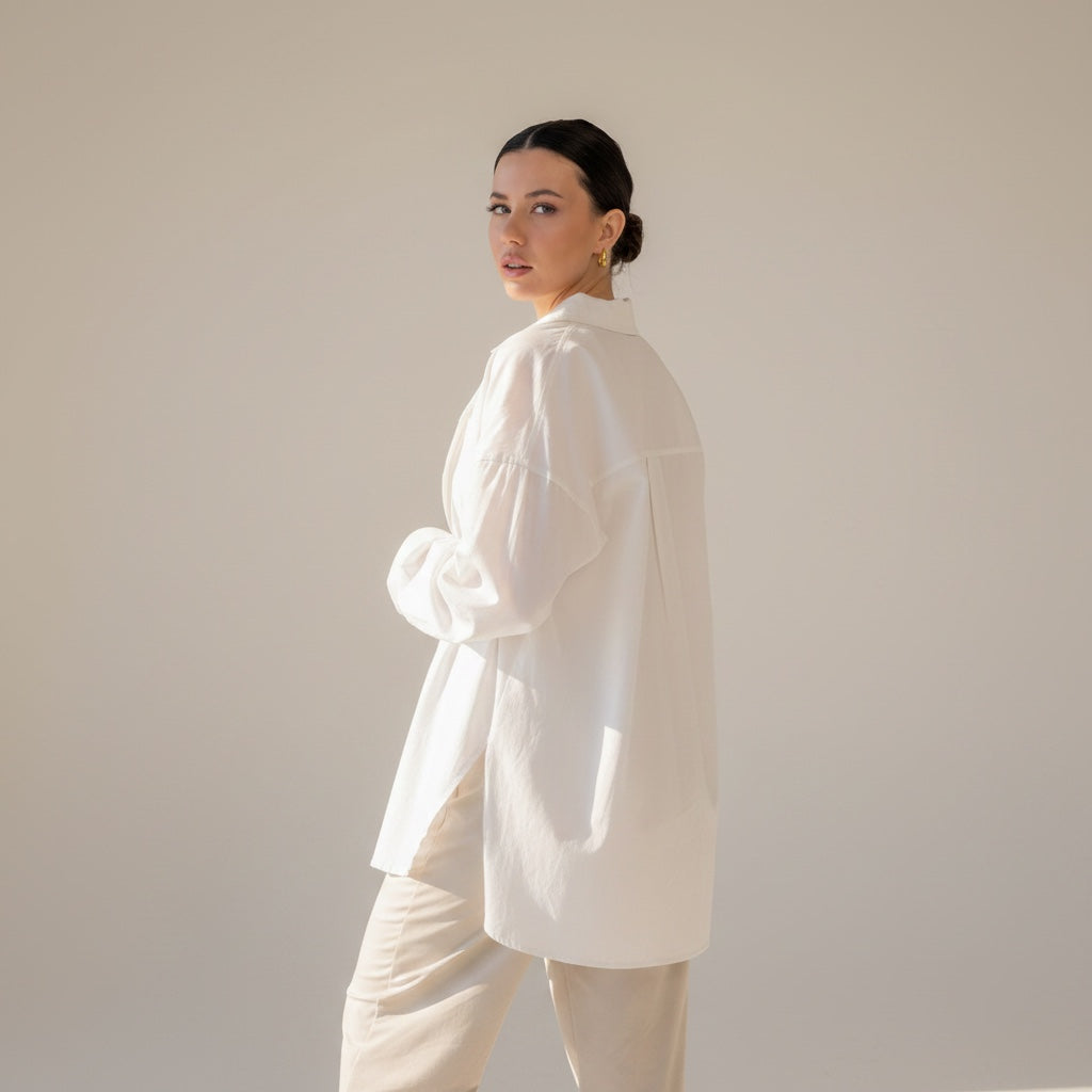 Model wearing an OKAKIE white cotton poplin boyfriend over-shirt with a high-low hem and side slits