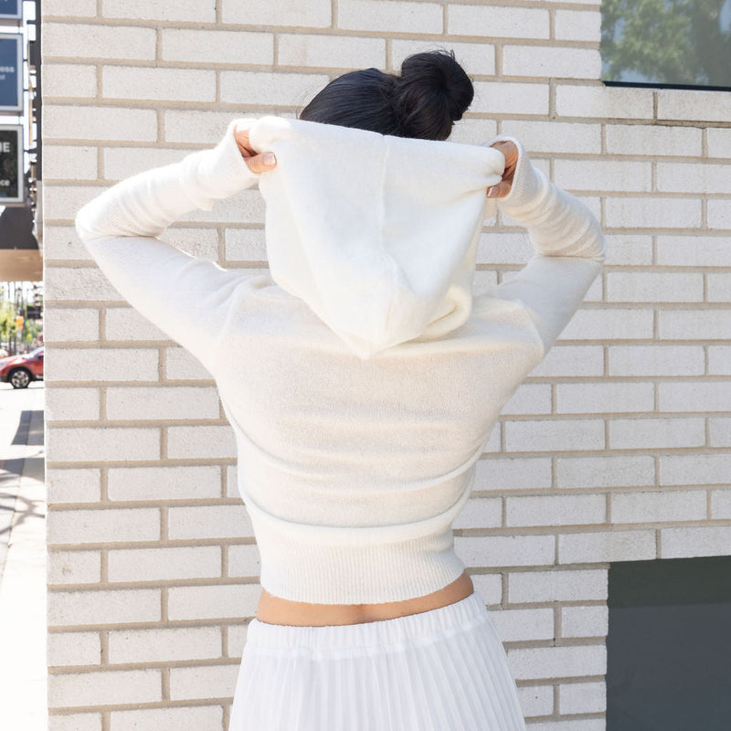 OKAKIE white cotton knit zip hoodie with a relaxed fit and ribbed hem worn by a woman against a brick wall