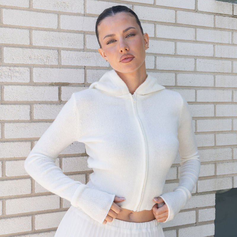 Model wearing OKAKIE white cotton-rich knit zip-up hoodie with long sleeves and a clean, fitted silhouette.