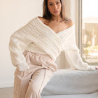 OKAKIE white cable knit sweater with a criss cross adjustable V-neckline and dolman sleeves worn off-shoulder