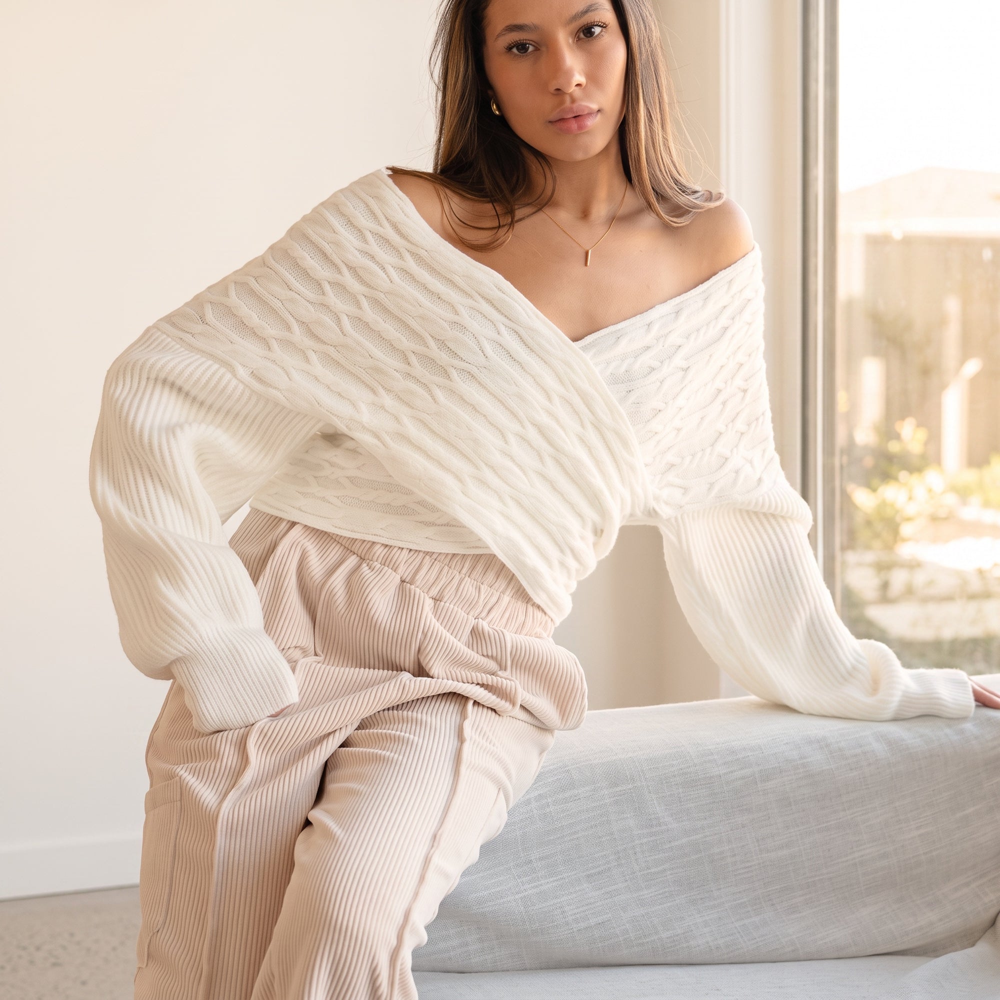 OKAKIE white cable knit sweater with a criss cross adjustable V-neckline and dolman sleeves worn off-shoulder