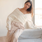 OKAKIE white cable knit sweater with a criss-cross off-shoulder design and wide dolman sleeves worn by a model