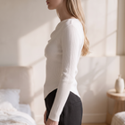 OKAKIE Éliora white ribbed sweater top with an asymmetric draped neckline and long fitted sleeves on a model.