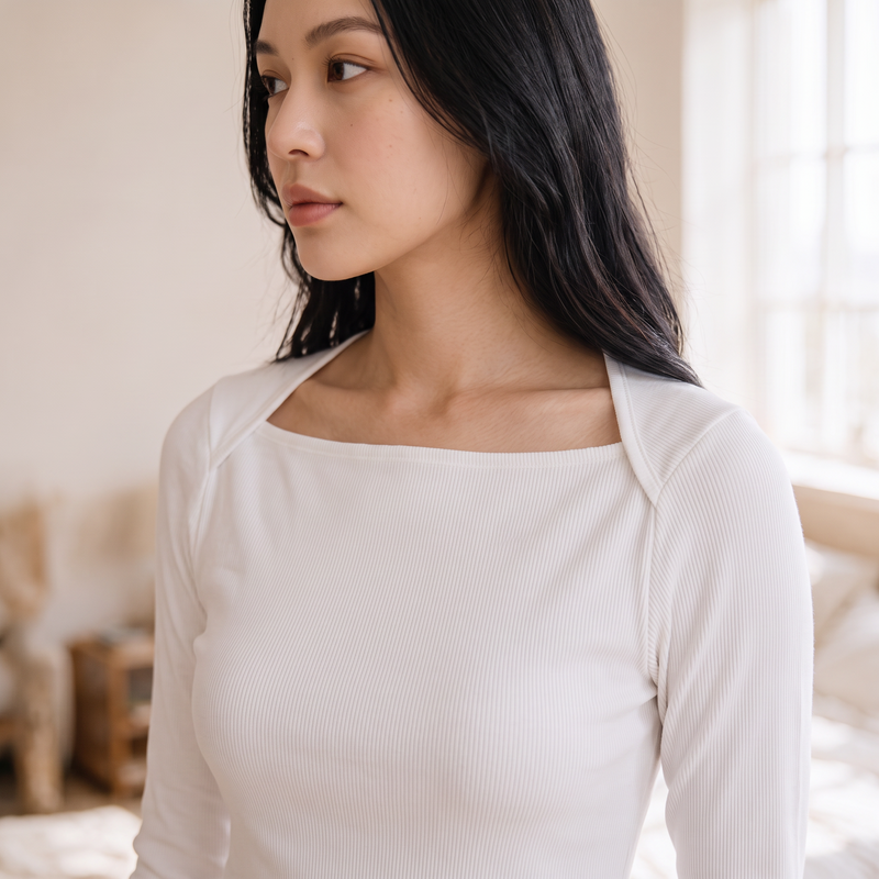 OKAKIE white square neck rib knit top with long sleeves worn by a woman in a bright, minimalist interior.